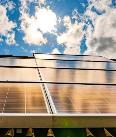 Paneles solares instalados en un techo que reflejan la luz del sol con un cielo parcialmente nublado de fondo, marcando el inicio de un viaje energético ecológico.