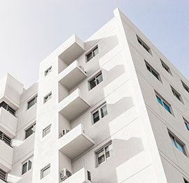 Una vista de ángulo bajo de un edificio residencial blanco de varios pisos con varios pequeños balcones y ventanas contra un cielo despejado..