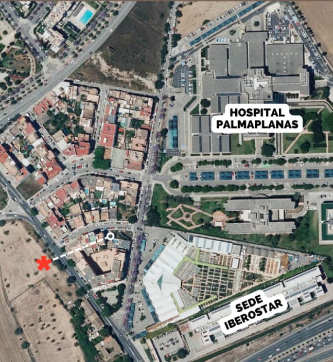 Vista aérea de una zona de la ciudad con el Hospital Palmaplanas y la Sede Iberostar rotulados. Una X roja marca una ubicación no especificada cerca de una zona residencial y terreno abierto, potencialmente de interés para cualquier promotora que busque oportunidades de desarrollo.